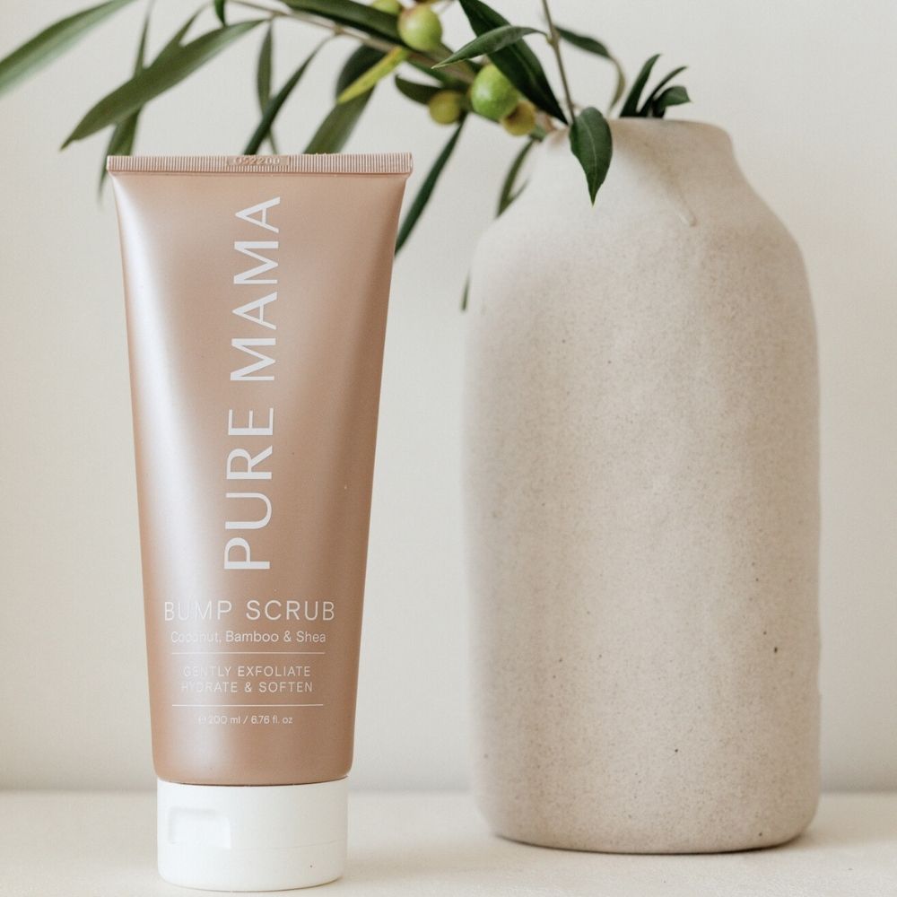 A copper-colored tube of Pure Mama NZs Mama & Baby Set, a pregnancy skincare essential, stands near a beige ceramic vase with leafy branches. Its white text and softly blurred background highlight the products natural and organic ingredients.